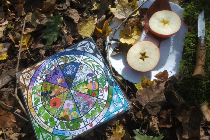 Autel de Samhain comprenant une roue des saisons, une pomme coupée en deux montrant le pentacle contenant les graines. Le tout sur un sol de feuilles d'automne.